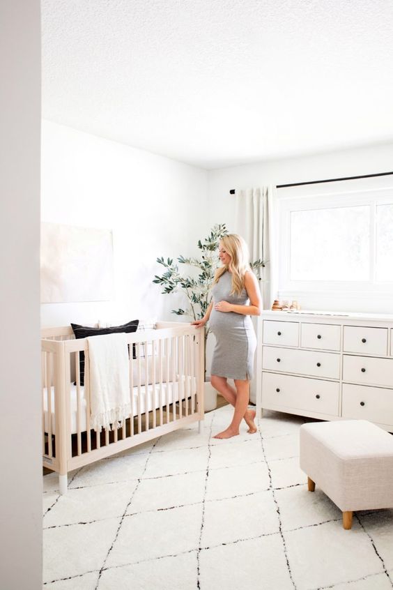 an airy neutral nursery with neutral furniture, a printed rug, a statement plant and neutral textiles is a cozy space