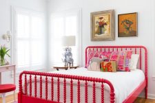 an artistic bedroom with a bold red vintage bed and a stool, chic artworks, a table lamp with elephants and a vintage chandelier