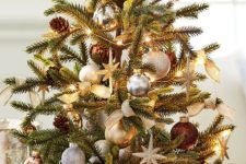 an elegant tabletop Christmas tree with lights, silver, gold and brown ornaments, burlap bows and pinecones