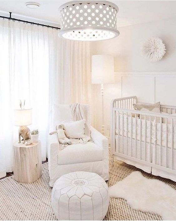 an ethereal neutral nursery with a paneled wall, some vintage furniture, a pendant lamp, white textiles and a tree stump side table
