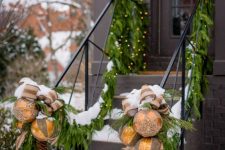 05 outdoor railing decor with lush fir branches, lights, oversized gold ornaments with bows and pinecones is lovely