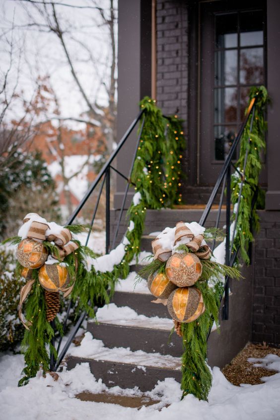 outdoor railing decor with lush fir branches, lights, oversized gold ornaments with bows and pinecones is lovely