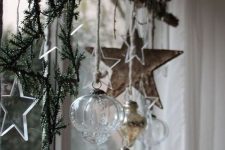 21 Nordic Christmas window decor with fir branches, a wooden star, sheer and silver ornaments, sheer stars and lights
