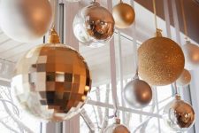 23 white, gold and silver Christmas ornaments of various sizes hanging on the window for chic holiday decor