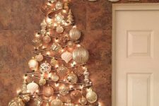 32 a wall-mounted Christmas tree of lights and white, copper and gold ornaments of various sizes and some pinecones and faux blooms