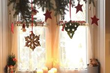 Christmas window decor with an evergreen branch, red stars and some gingerbread cookies is a catchy and cozy Christmas decor idea