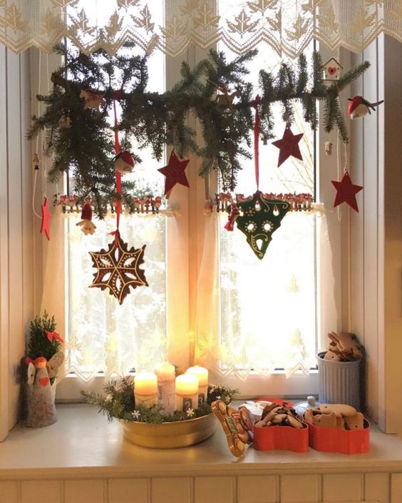 Christmas window decor with an evergreen branch, red stars and some gingerbread cookies is a catchy and cozy Christmas decor idea