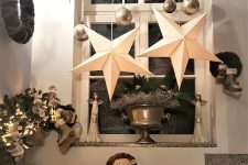 Christmas window decor with silver ornaments, clear stars, greenery and large star lamps is super catchy