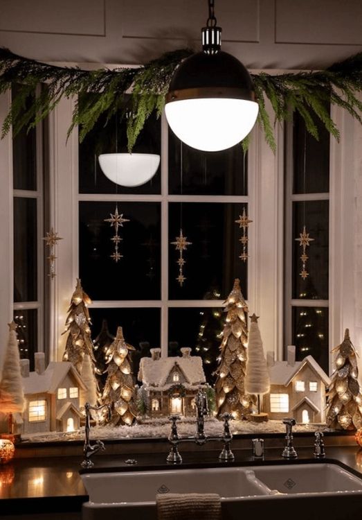 Christmas window decor with stars and evergreens, houses and Christmas trees with lights inside
