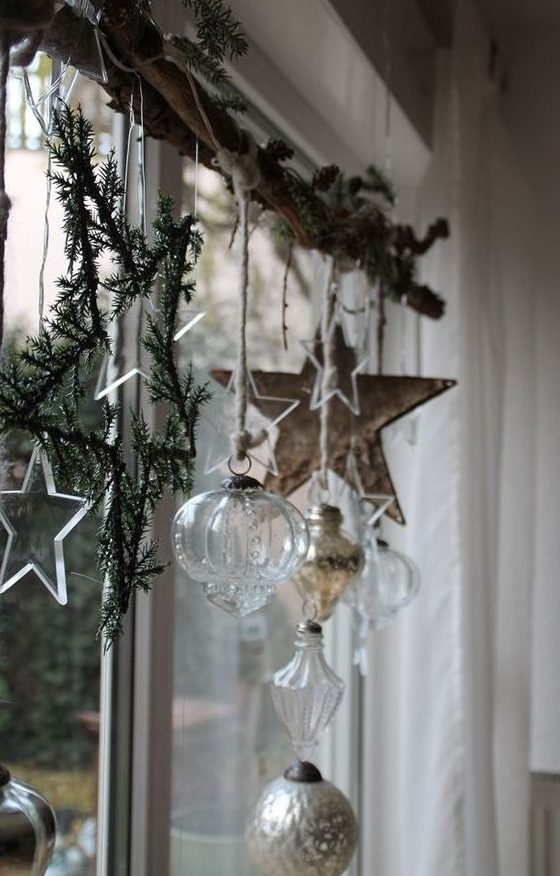Nordic Christmas window decor with fir branches, a wooden star, sheer and silver ornaments, sheer stars and lights