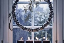 Nordic window decor with a bell wreath with twigs, pillar candles and pinecones looks amazing and very natural