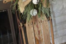 a Christmas decoration of a sleigh with a burlap bow, some berries, faux greenery and large white bells is a cozy vintage decor idea