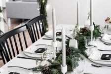 a Nordic Christmas table with a fir runner with pinecones, grey candles, white porcelain and printed napkins and cookies on a plate