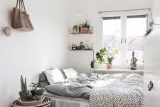 a Scandinavian bedroom with a bed and printed bedding, a woven bedside table, some shelves, a chandelier and some plants