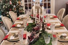 a beautiful Christmas tablescape with burlap placemats, fir branches with berries and pinecones, candles, gold cutlery and chargers