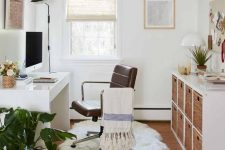 a boho home office with a desk, a leather chair, a storage unit with baskets, some potted plants and artwork