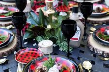 a bold Christmas tablescape with plaid plates and red candles, evergreens and magnolia leaves plus black napkins and glasses