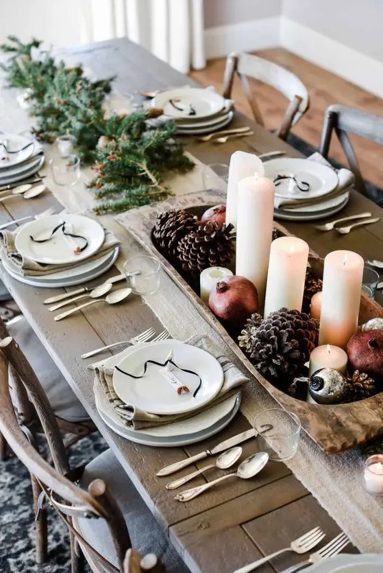 a bold farmhouse Christmas tablescape with evergreens, a wooden bowl with pinecones, pomegranates and pillar candles, neutral linens