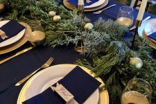 a bold modern Christmas tablescape with gold chargers and cutlery, ornaments and candleholders, navy linens is wow