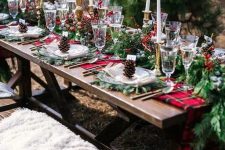 a bold outdoor Christmas tablescape with an evergreen and red plaid runner, evergreen placemats, tall and thin candles, berries on the table and some pinecones