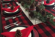 a bold rustic Christmas tablescape with a plaid tablecloth, red napkins, black and white plates, pinecones and evergreens