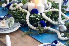 a bold white and navy Christmas tablescape with a blue runner, navy bows and ornaments, candles, beads, wooden plates and plaid napkins
