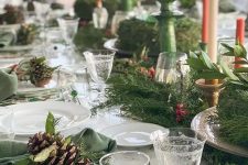 a bright Christmas tablescape with printed placemats, printed plates, an evergreen runner with berries, colored candles in green candleholders