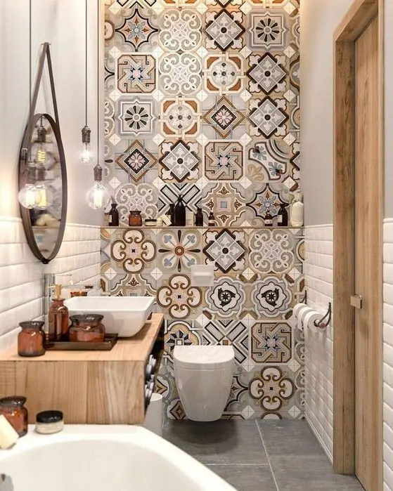 a bright and small bathroom with a mosaic tile wall, a floating wooden vanity, a tub, a round mirror and bulbs