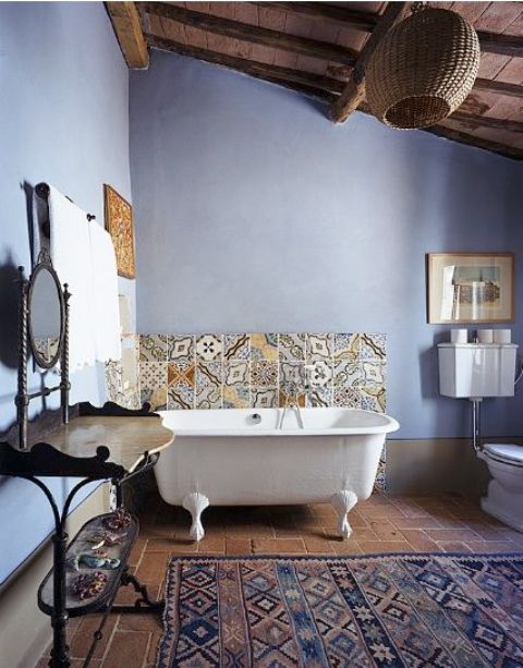 a bright boho and vintage bathroom with a clawfoot tub, bright pritned tiles over it, a boho rug, a vintage table and a mirror