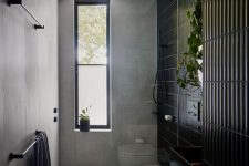 a catchy bathroom with grey stone tiles and black skinny ones, a shower space, a vanity with a black sink
