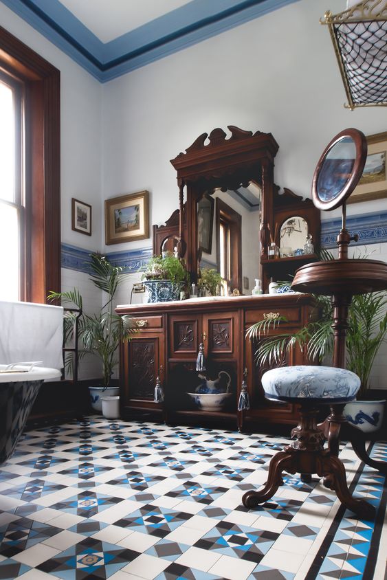 a catchy vintage bathroom with blue tiles on the floor and walls, heavy wooden furniture with blue upholstery and vintage touches