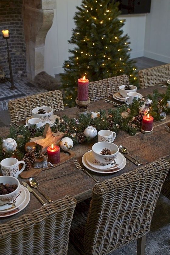 a chic Christmas tablescape with an evergreen and ornament runner, pillar candles, wooden stars and pinecones