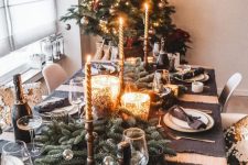 a chic and glam Christmas tablescape with black placemats, fir branches, gold candles, black napkins is very elegant