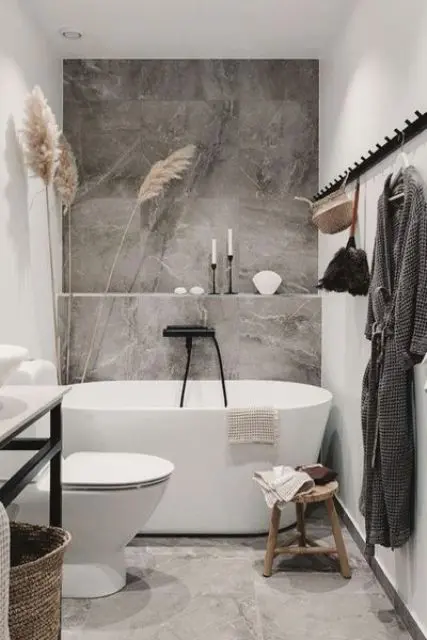 a chic contemporary bathroom with grey stone tiles, an oval tub, a vanity with a sink, a rack and pampas grass