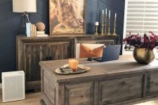 a chic modern farmhouse home office with a navy paneled wall, a heavy stained desk and a cabinet, some candles, a table lamp and a cool pendant one