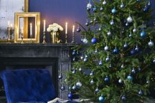 a christmas tree with silver, bold blue and navy ornaments plus navy furniture and walls for a monochromatic holiday space