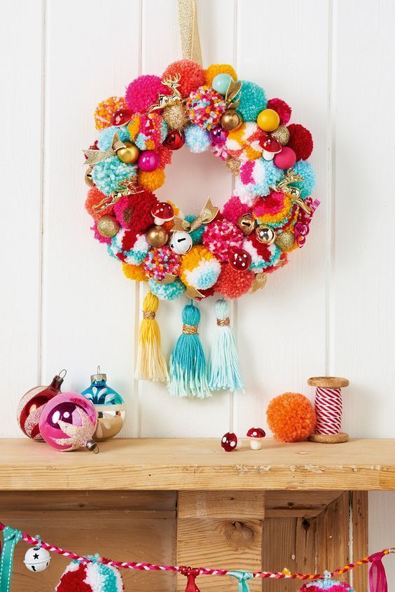 a colorful pompom wreath with bright bells and gold bows plus colorful tassels and a deer is lovely for the holidays