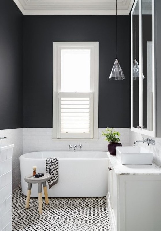 a contrasting bathroom with black and white walls, a mosaic floor, an oval tub, a stool and a glass cone pendant lamp