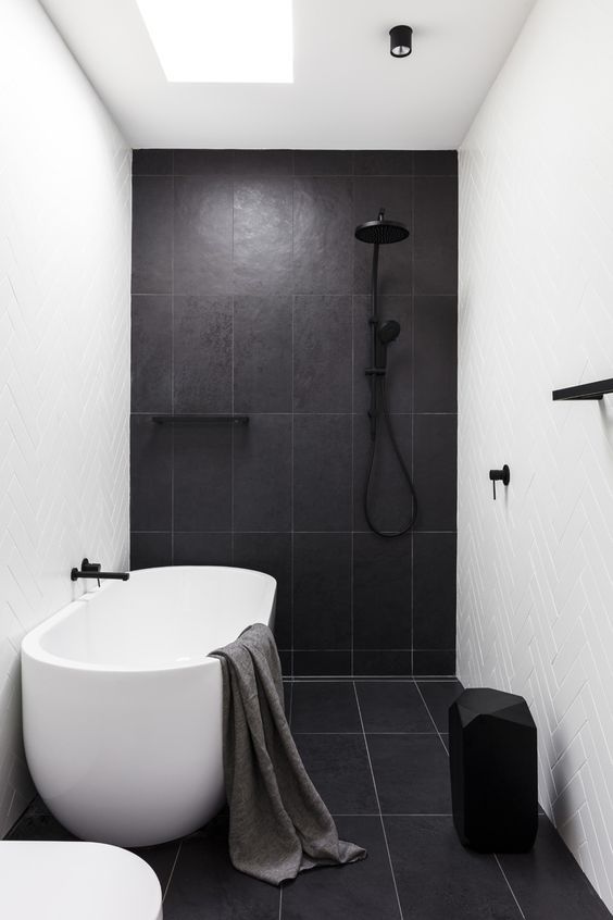 a contrasting bathroom with herringbone and large scale tiles, an oval tub, a black stool and black fixtures