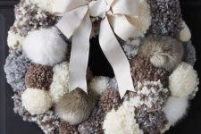 a cozy neutral pompom and faux fur wreath with a large bow is a very warming and cool decoration for your front door