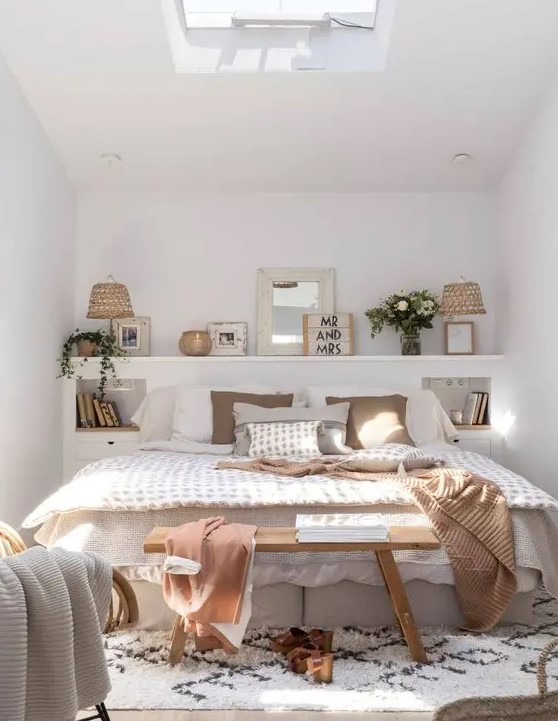 A cozy small boho bedroom with a ledge with decor and lamps, a bed with neutral bedding, built in nightstands and a printed rug