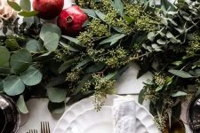 a cute and chic Christmas tablescape with a lush greenery runner, pomegranates, white porcelain and gold cutlery