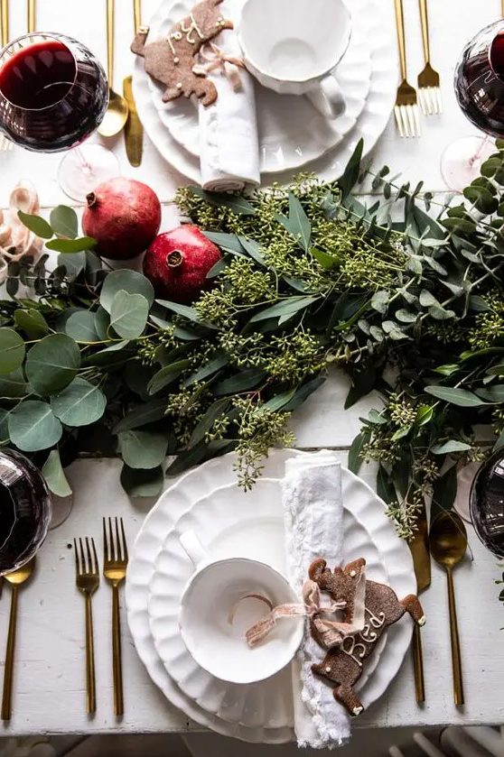 a cute and chic Christmas tablescape with a lush greenery runner, pomegranates, white porcelain and gold cutlery