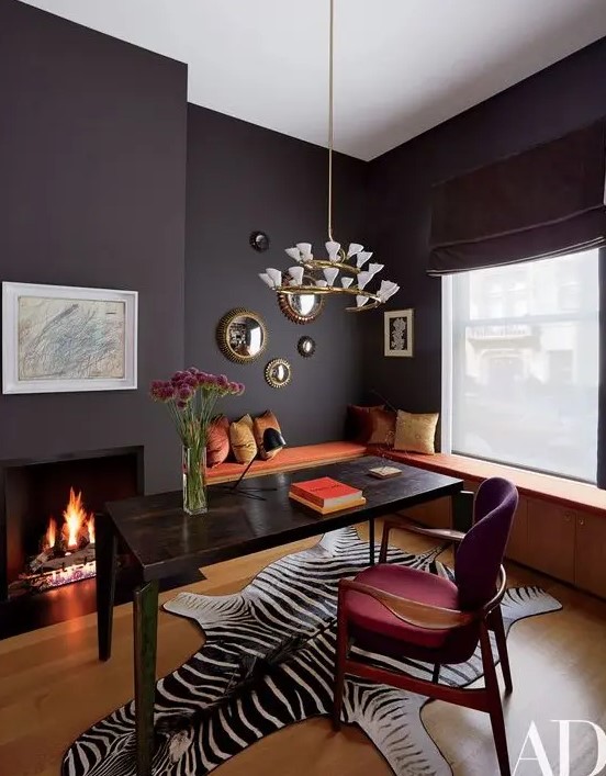 A fancy home office with a storage windowsill seating, a black desk, a fuchsia chair, a built in fireplace and a lovely chandelier