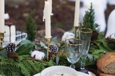 a farmhouse Christmas tablescape with an evergreen runner, cotton and snowy pinecones, tall and thin candles and white porcelain