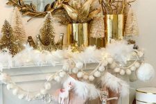 a glam Christmas mantel with whit fur, pink stockings, pompoms, gold tinsel trees, gold vases with leaves and branches