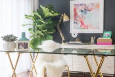 a glam feminine home office with a grey statement wall, a glass desk, a crystal chandelier and touches of gold