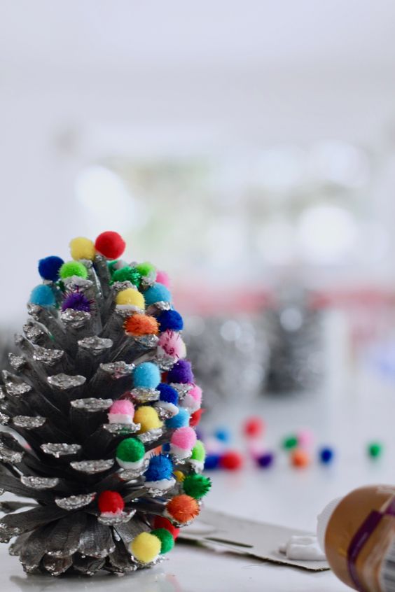 a glitter pinecone with colorful pompoms that add color and fun to it and make it look like a Christmas tree