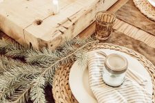 a hygge Christmas table with woven chargers, fir branches, a wooden board with candles, colored glasses is very peaceful