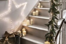 a hygge-like Christmas staircase with pillar candles, light stars over the stairs and a fir and foliage garland with lights on the rails
